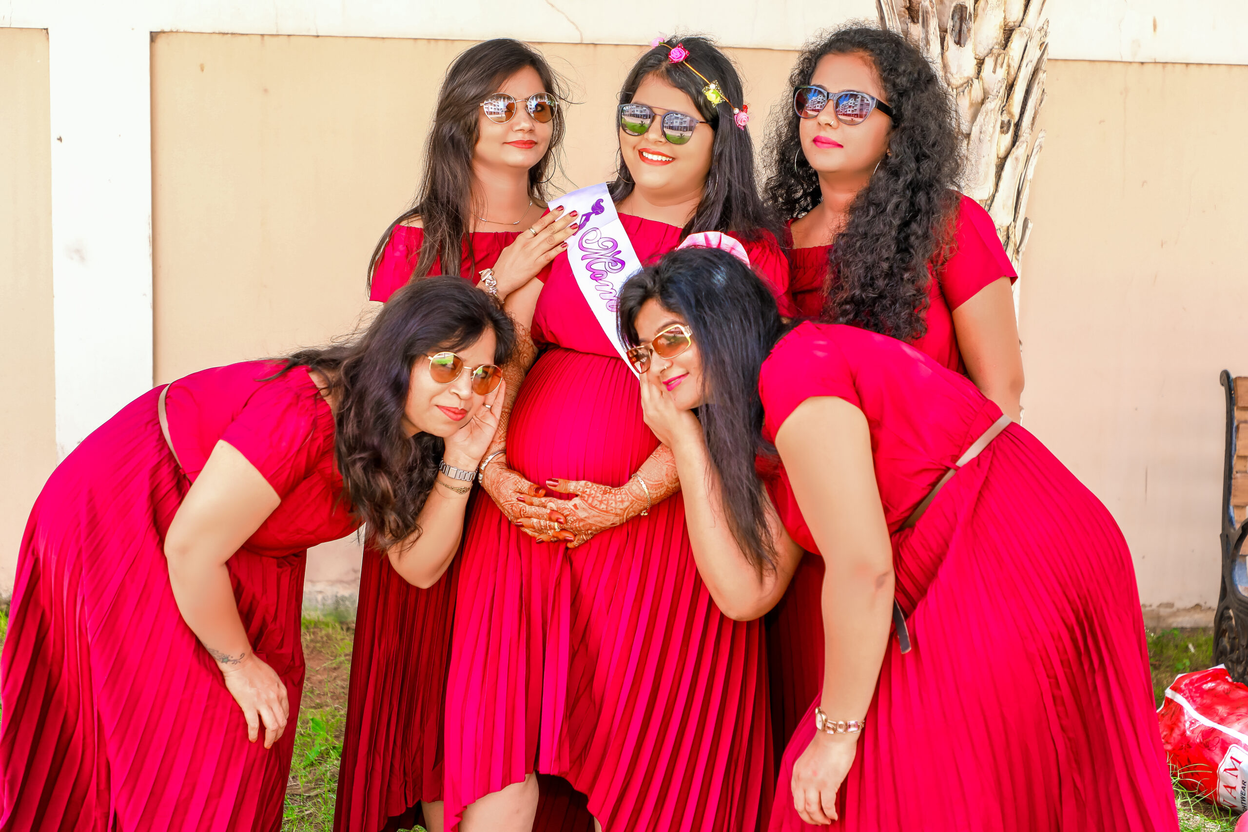 A group of women in red dresses posing for a picture during a maternity shoot by AK Photography Coimbatore
