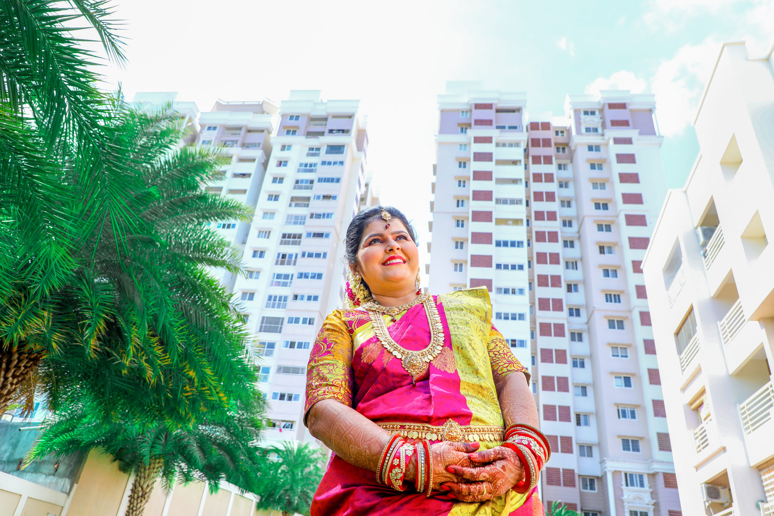 A woman in traditional Indian attire poses in front of tall buildings during Gayathri's Maternity Photoshoot by AK Photography Coimbatore.