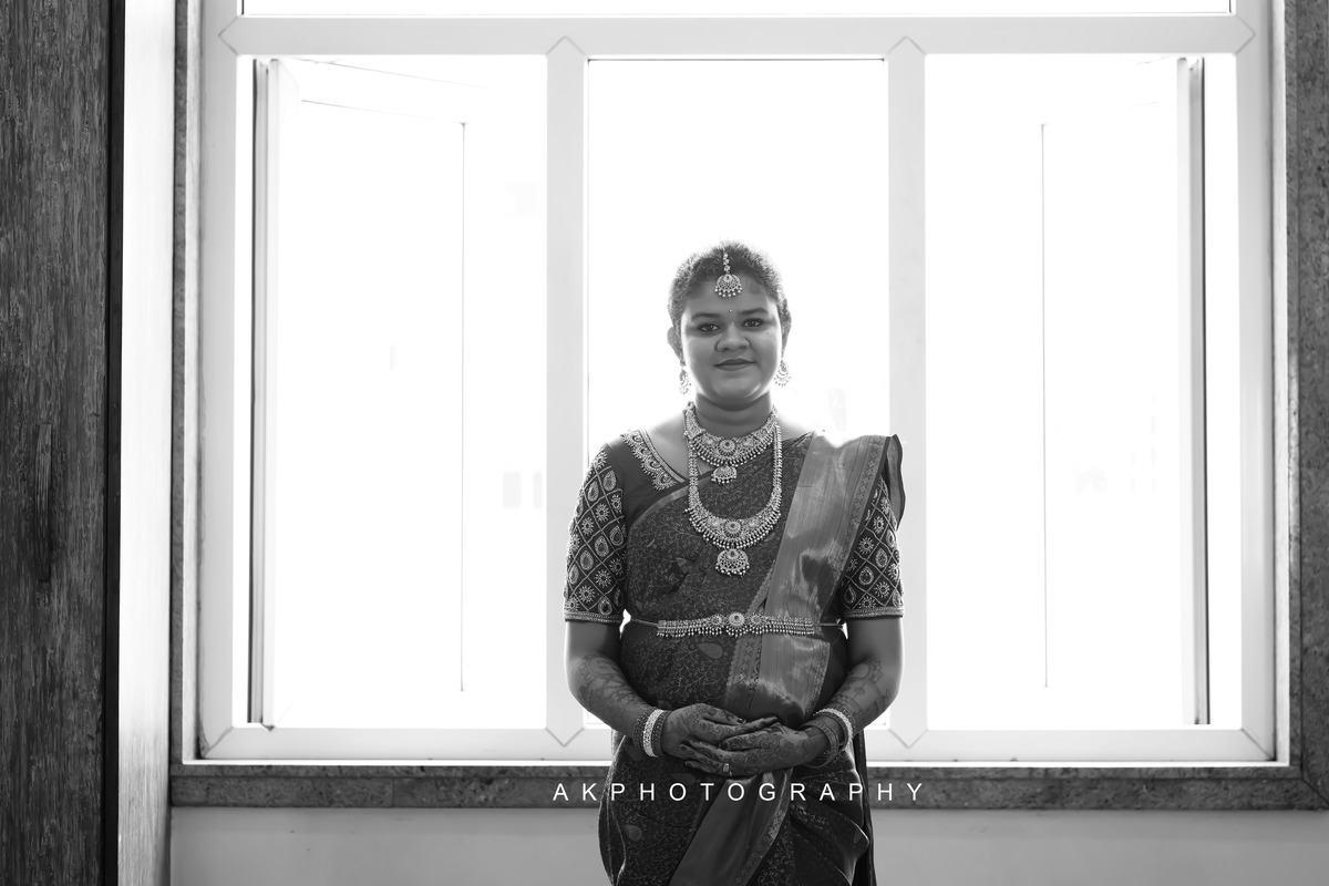 A bride in traditional Indian attire stands in front of a window during a Baby Shower Photoshoot by AK Photography.