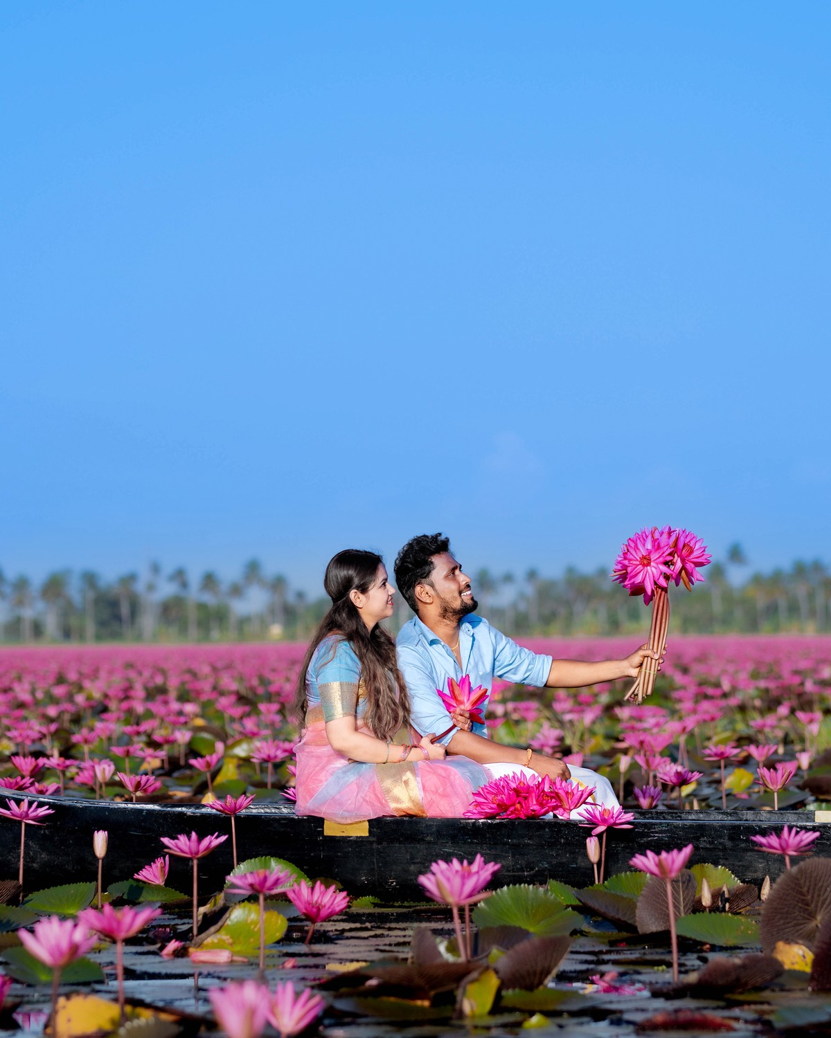 Wide scenic couple portrait of Shneka and Deepak in endless pink water lily fields at Malarikal Kerala by AK Photography