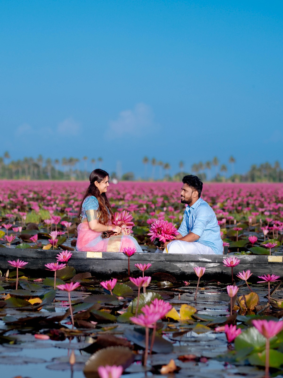 Romantic eye contact couple portrait of Shneka and Deepak framed by pink water lilies and coconut palms in Malarikal